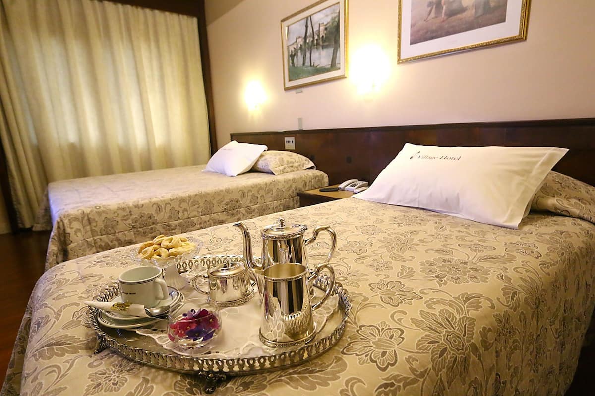 A hotel room with two beds, a tray with tea set, and a framed picture on the wall.