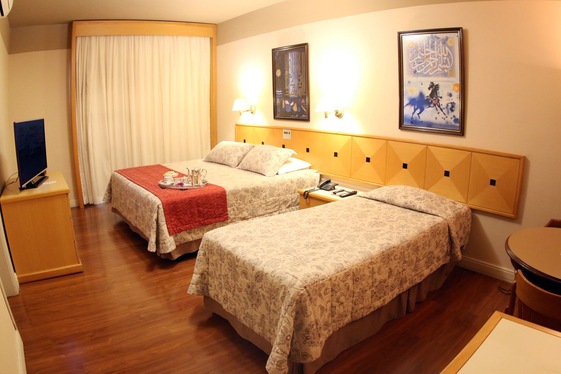 A hotel room with two beds, a TV, a telephone, and artwork on the wall.