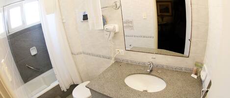 Un baño con lavamanos de granito, inodoro blanco y zona de ducha.