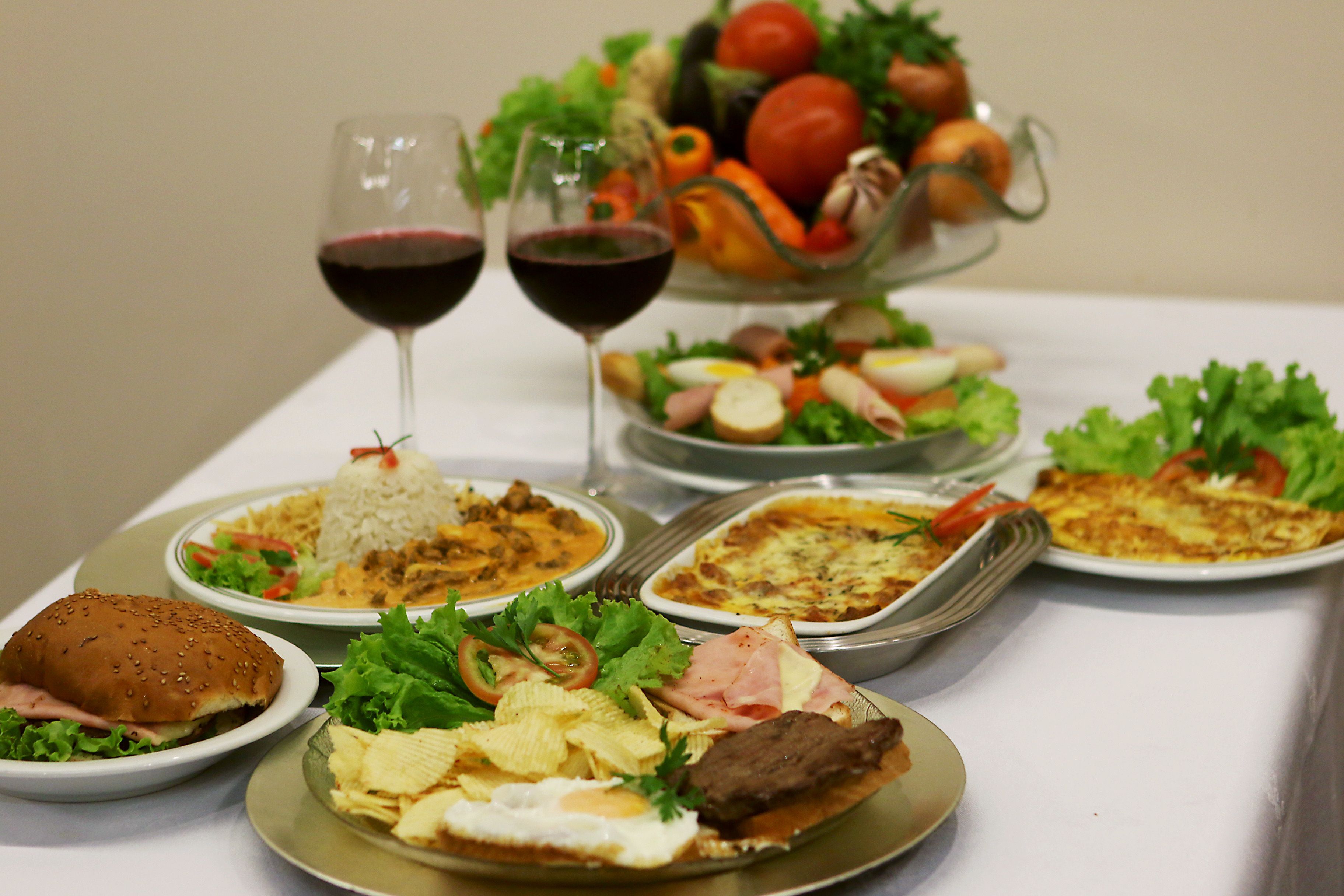 Una mesa dispuesta con diversos platos, incluyendo una hamburguesa, ensalada y un plato con huevos y papas fritas.