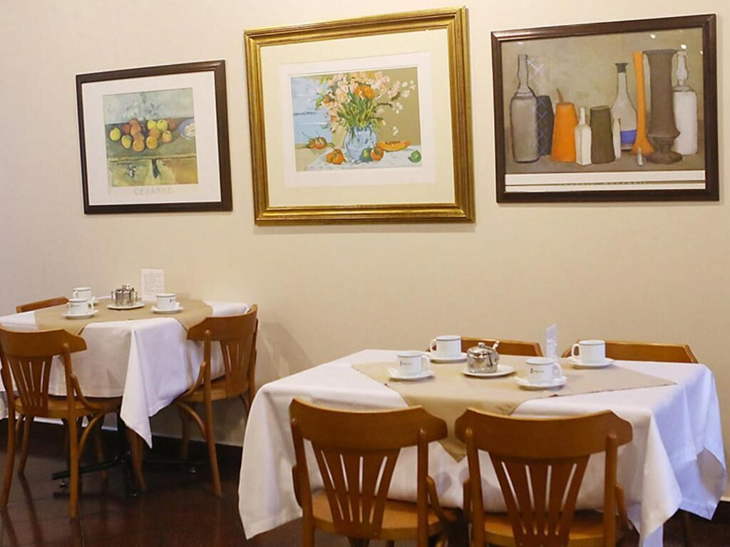 A dining area with tables set for two, framed artwork on the wall, and wooden chairs.