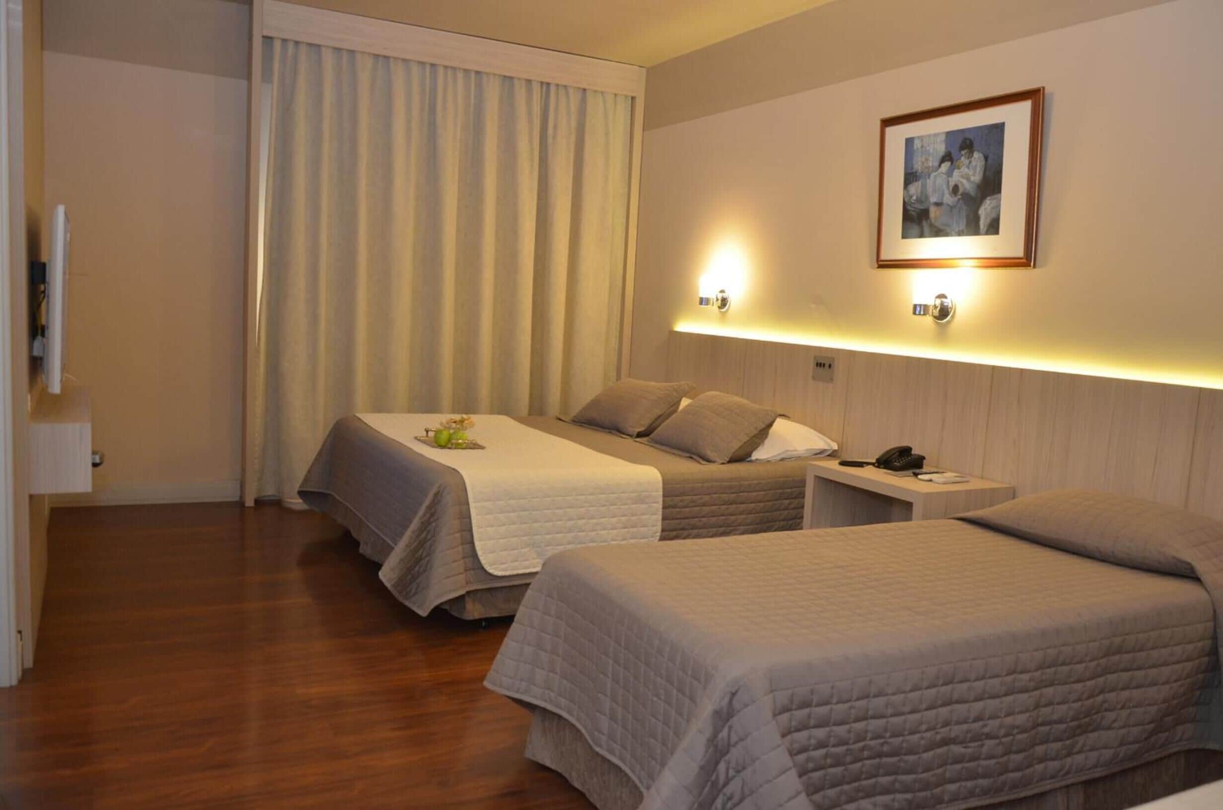 A hotel room with two beds, a bedside table with a phone, and a wall-mounted light fixture.