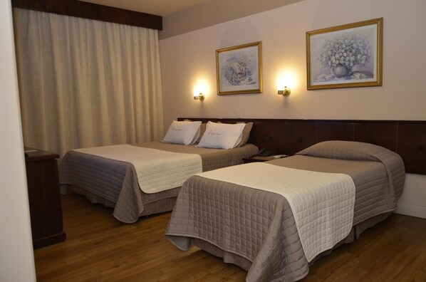 A hotel room with two beds, wooden flooring, and two wall-mounted light fixtures. - Village Hotel (Ponta Grossa)