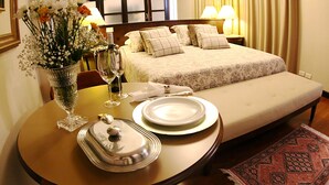 A hotel room with a bed, bedside lamps, a dining table with plates and a vase of flowers, and a window with curtains. - Village Hotel (Ponta Grossa)