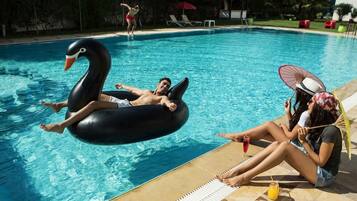 Una piscina con flotadores de cisne inflables, sillas de descanso y un deck de cerámica.