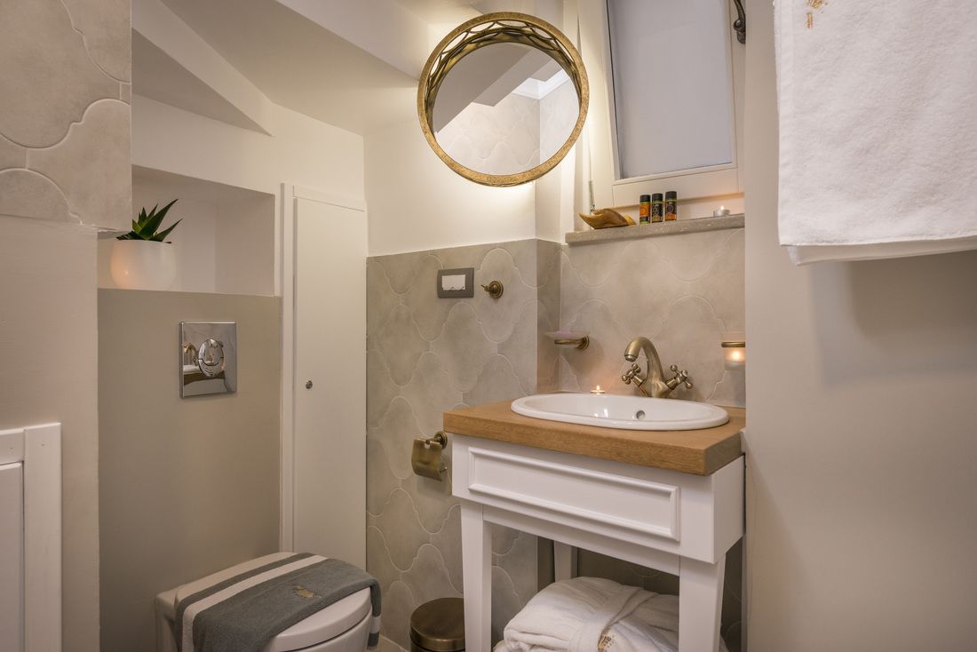 A bathroom with a white vanity, a round mirror, a towel rack, and a small plant.