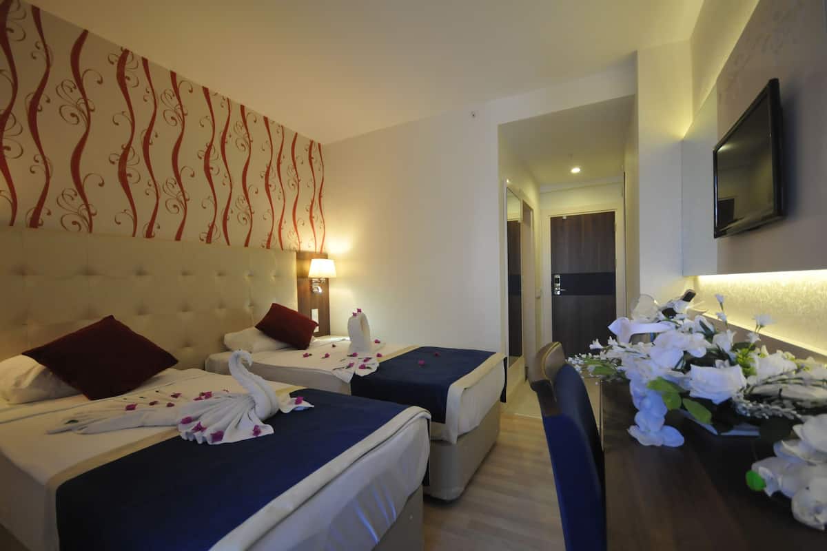 Habitación de hotel con dos camas, un tapiz grande en la pared, un televisor y un escritorio con flores.