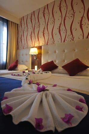 Habitación de hotel con una cama grande, dos almohadas rojas, cabecera blanca y una pared decorativa con remolinos rojos.