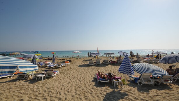 A beach with sun loungers and umbrellas, a clear sky, and the ocean in the background.