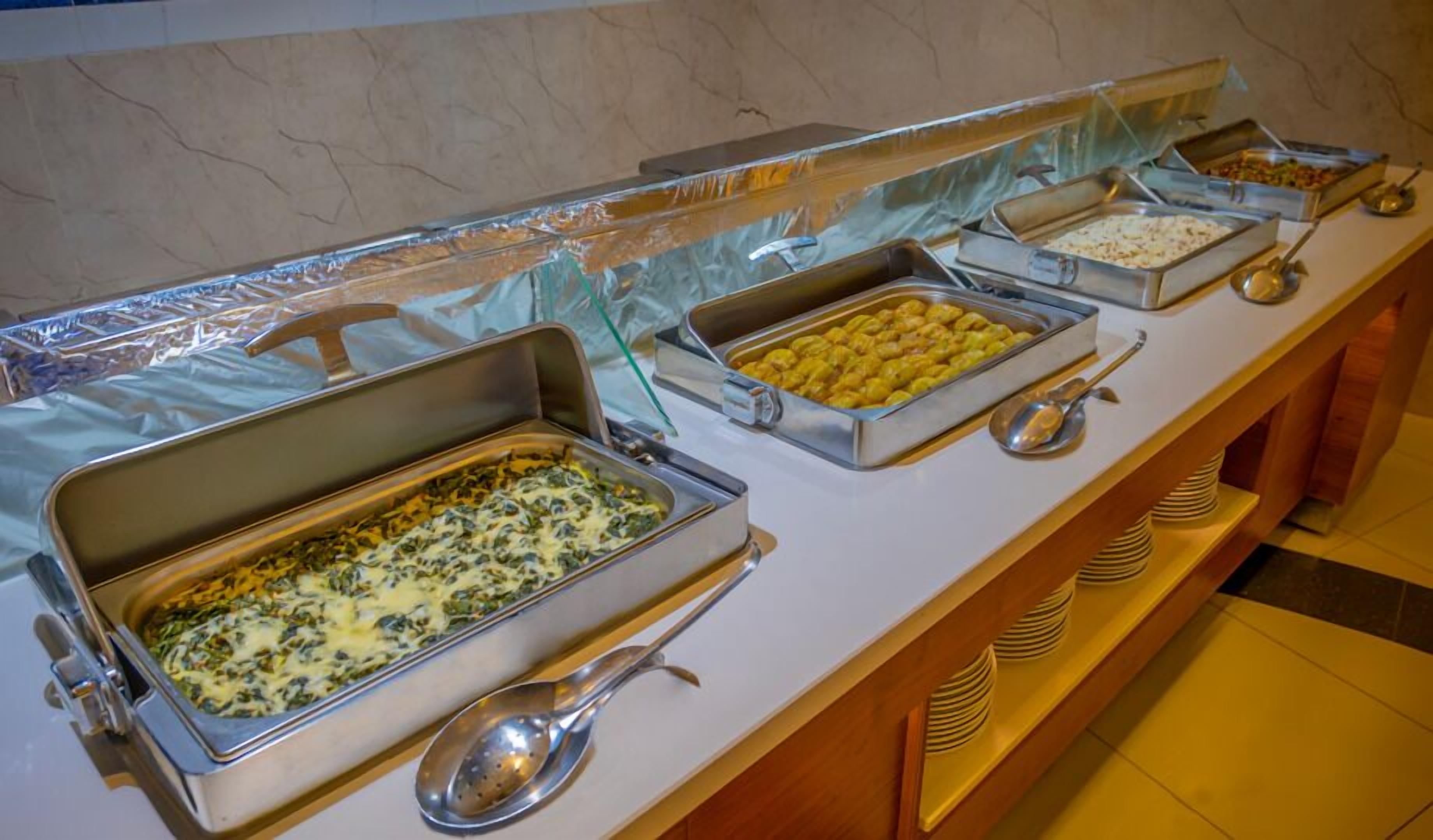 A buffet with various food items in metal containers, accompanied by serving spoons.