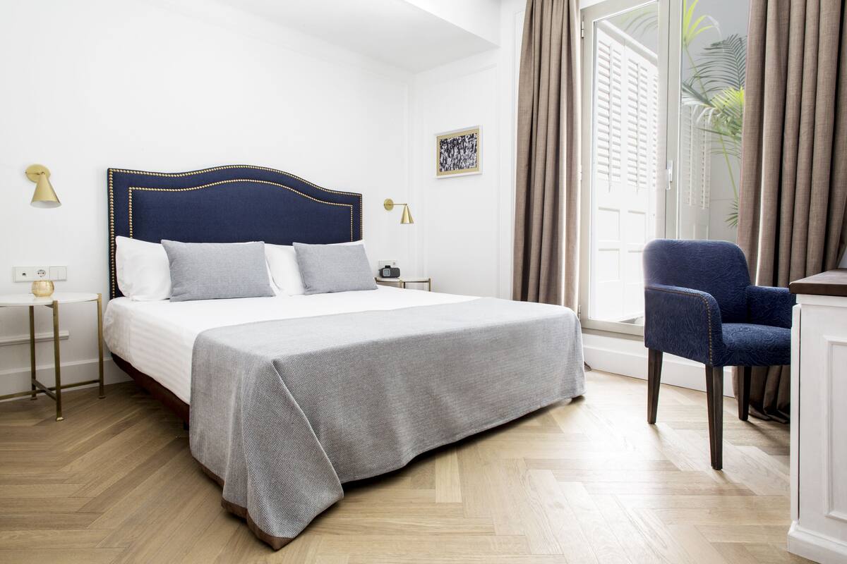 Une chambre d’hôtel bien aménagée, avec un lit, des tables de chevet, une chaise et une vue sur l’extérieur.