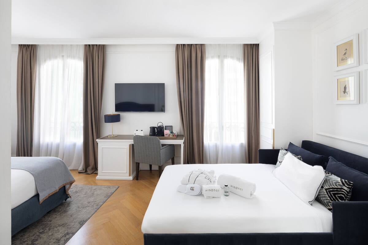 Une chambre d’hôtel avec un lit, un bureau, une chaise, une télévision et des rideaux.