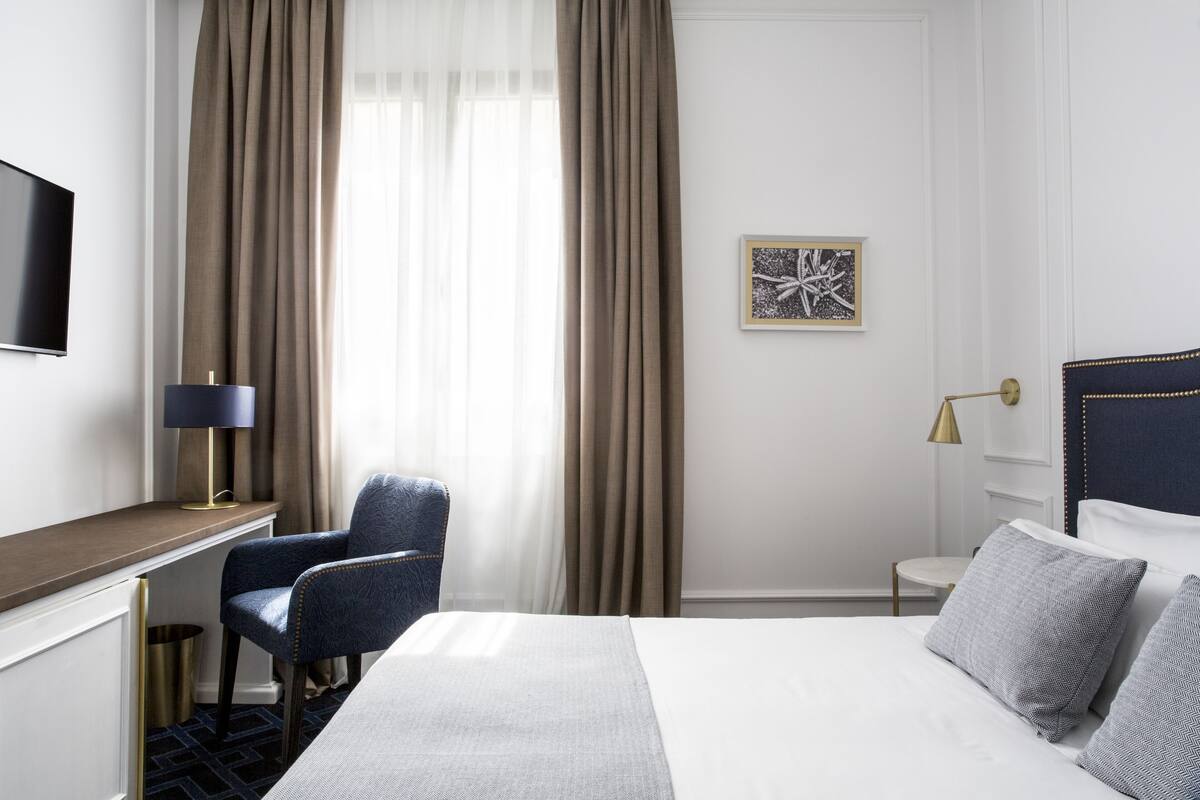 Une chambre d’hôtel équipée d’un lit, d’un bureau, d’une chaise, d’une télévision et d’une fenêtre avec des rideaux.