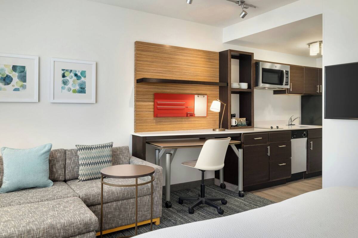 Een moderne hotelkamer met een bank, een klein rond tafeltje, een bureau met een stoel, een magnetron en een wastafel.