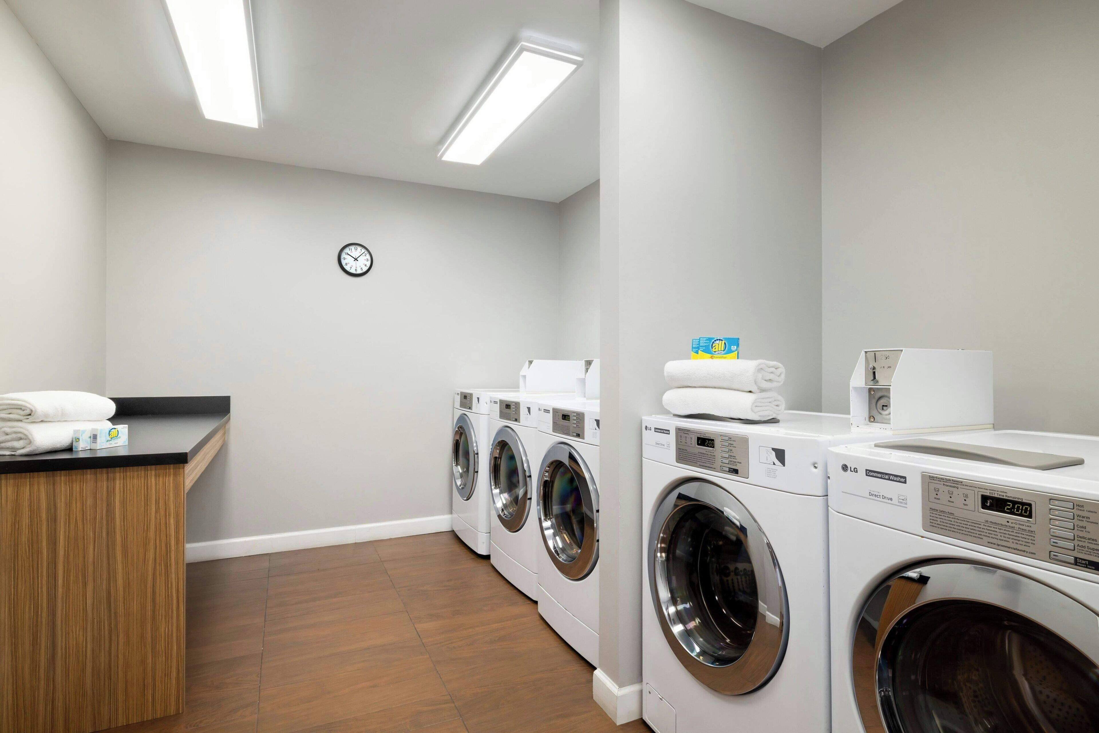 A laundry room with four front-loading washers and dryers, a wooden counter with towels, and a clock on the wall.