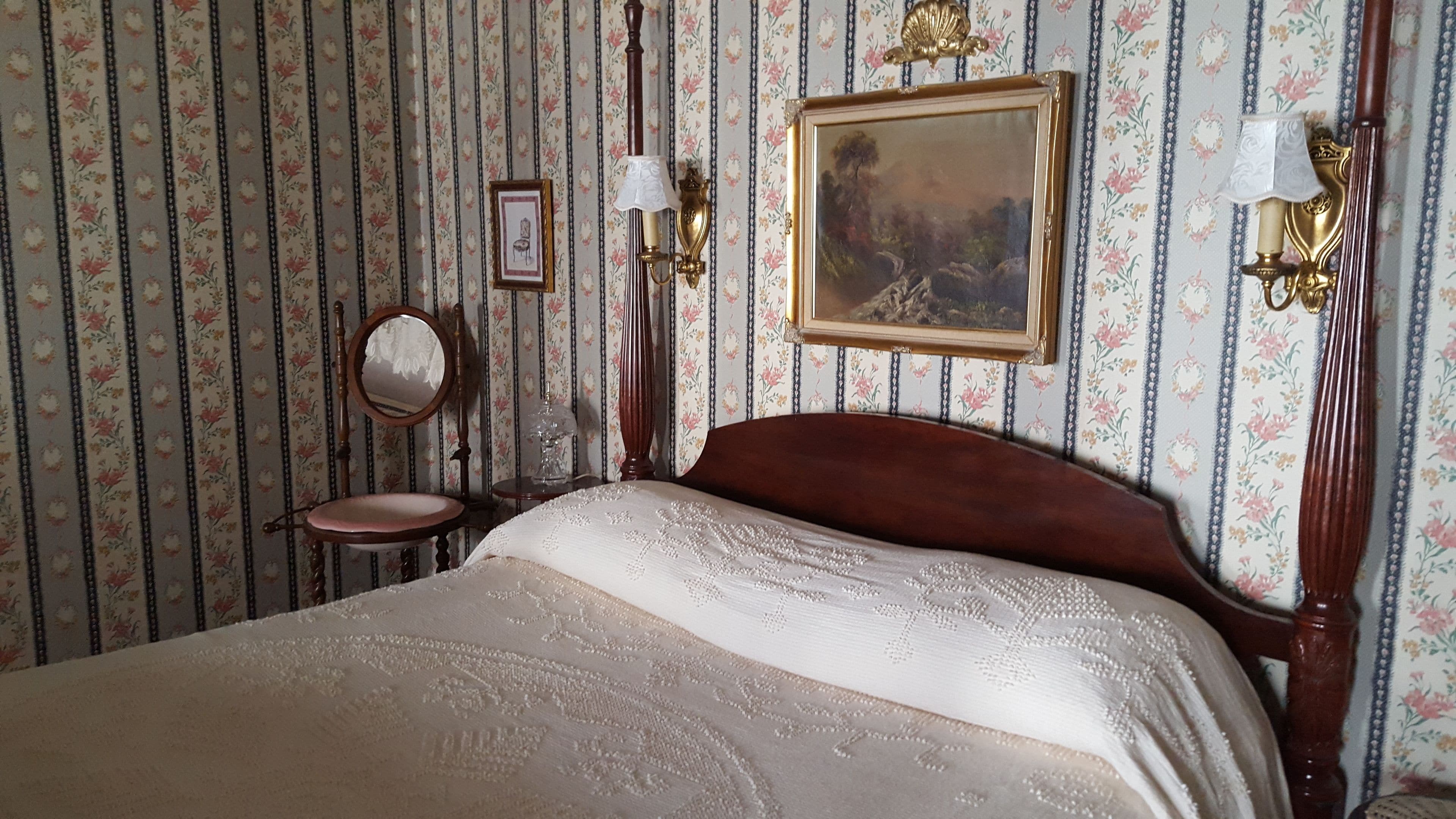 Una camera da letto con un letto grande, una sedia di legno, uno specchio tondo e un quadro appeso al muro.