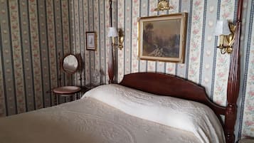 Una camera da letto con un letto grande, una sedia di legno, uno specchio tondo e un quadro appeso al muro.