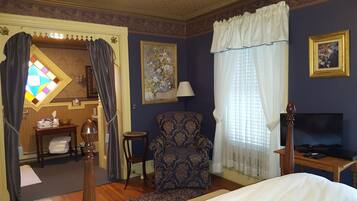Habitación de hotel con cama, una silla, televisor, lámpara, un cuadro y un vitral.