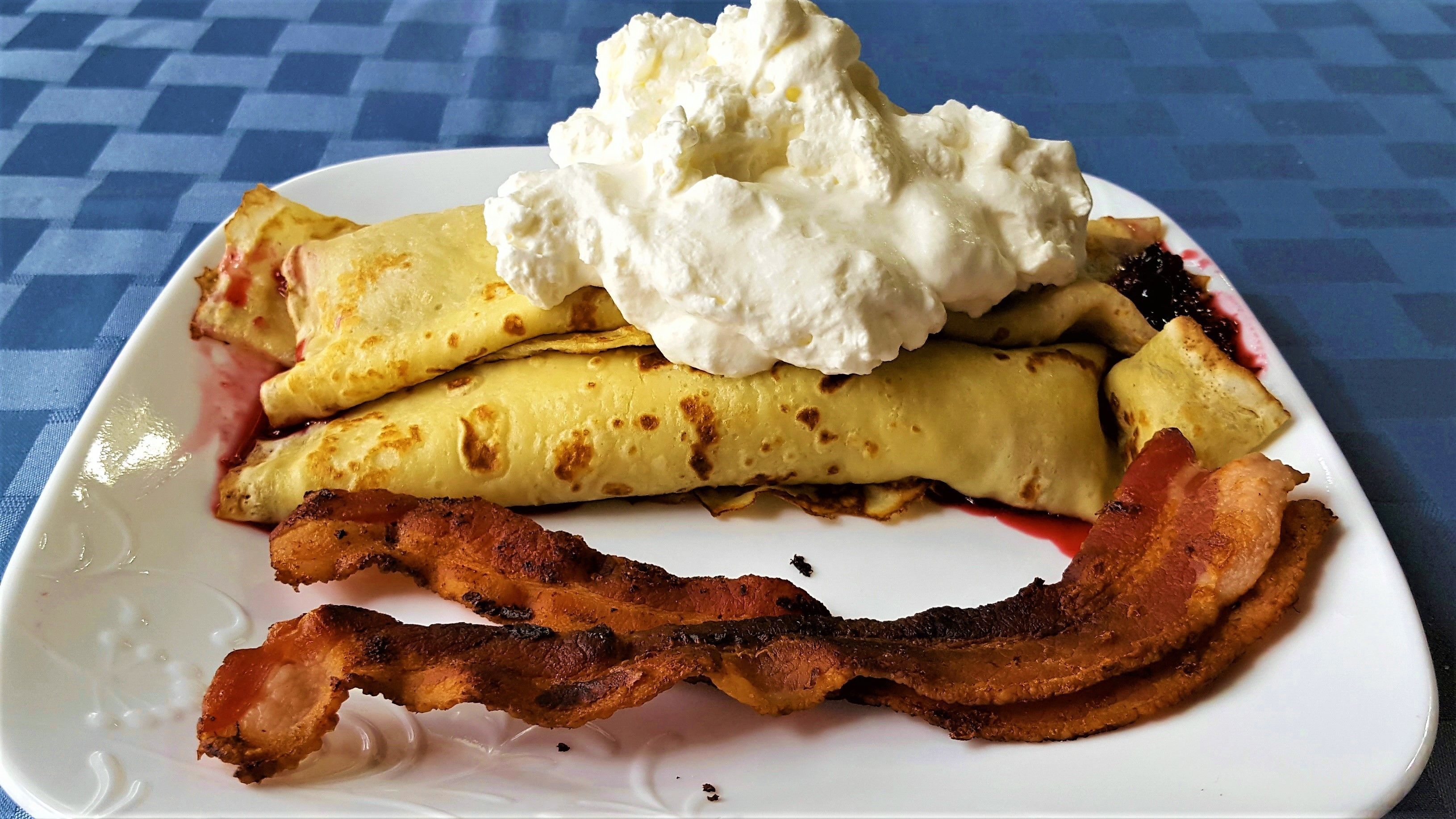 A plate with pancakes, whipped cream, and bacon.