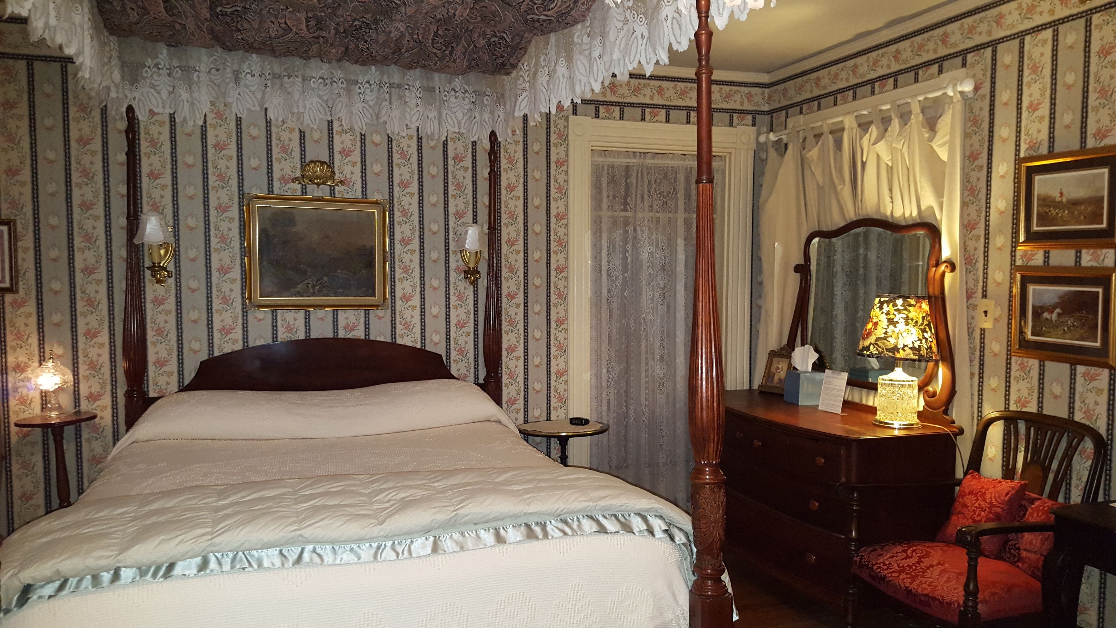 A bedroom with a four-poster bed, a dresser, a chair, and a mirror.