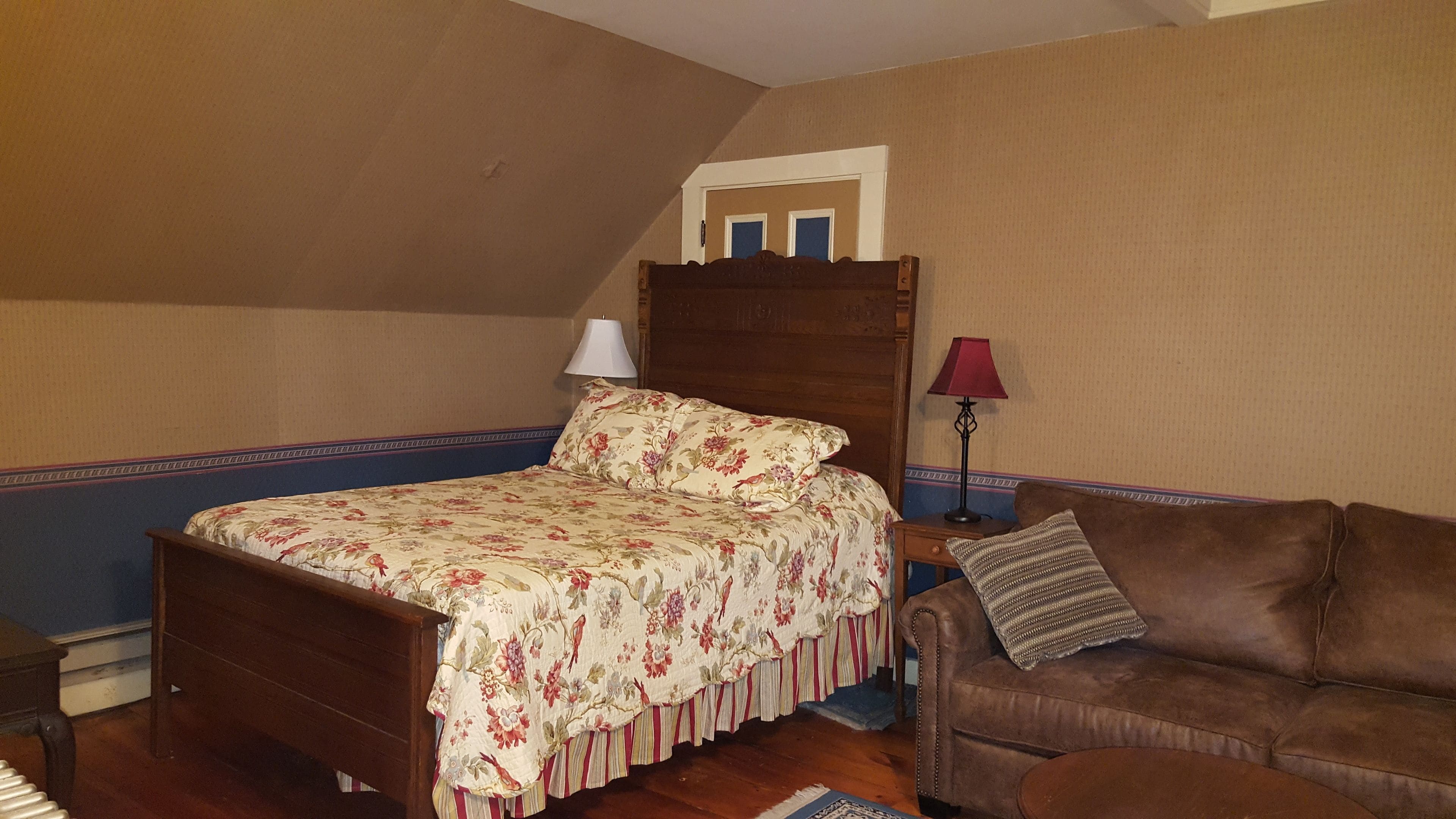 A bedroom with a wooden bed, a brown leather sofa, and a nightstand with a lamp.