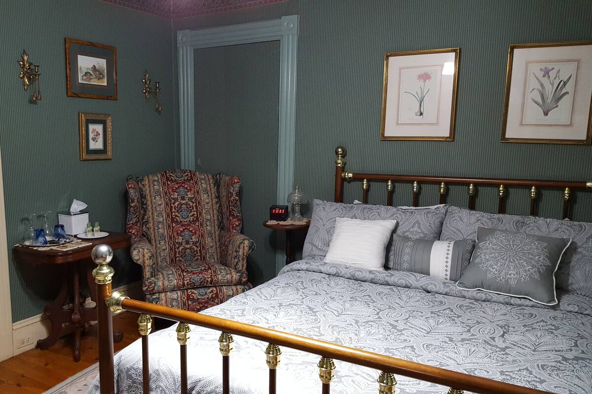 Un dormitorio con cama, una silla, una mesita de noche y cuadros en la pared.