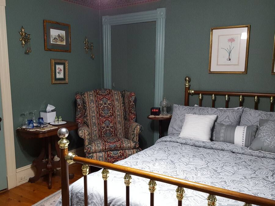 Une chambre à coucher avec un lit, une chaise, une table de chevet et des tableaux encadrés accrochés au mur.