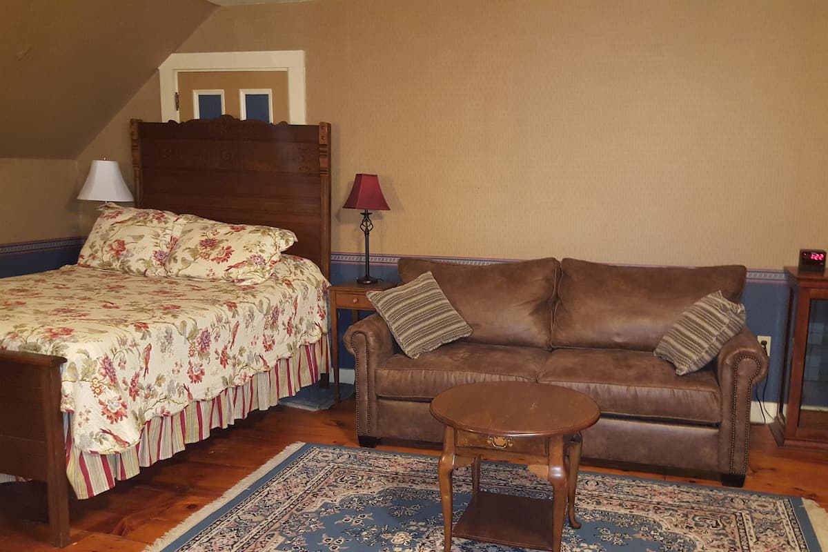 Un dormitorio con cama, sofá de cuero marrón, una mesita de madera y alfombra estampada.