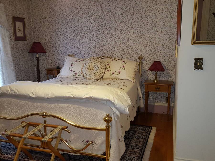 A bedroom with a bed, two bedside tables, a nightstand, a radiator, and a window with curtains.