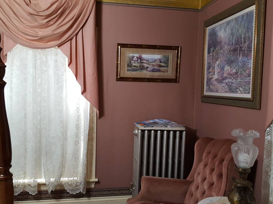 Una habitación con una cama con dosel de madera, un radiador, un cuadro de paisaje enmarco y un florero sobre una mesa.