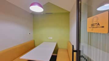 Una sala de reuniones con una mesa blanca, asientos acolchados amarillos, un separador de vidrio y un letrero que indica que es la sala 903.