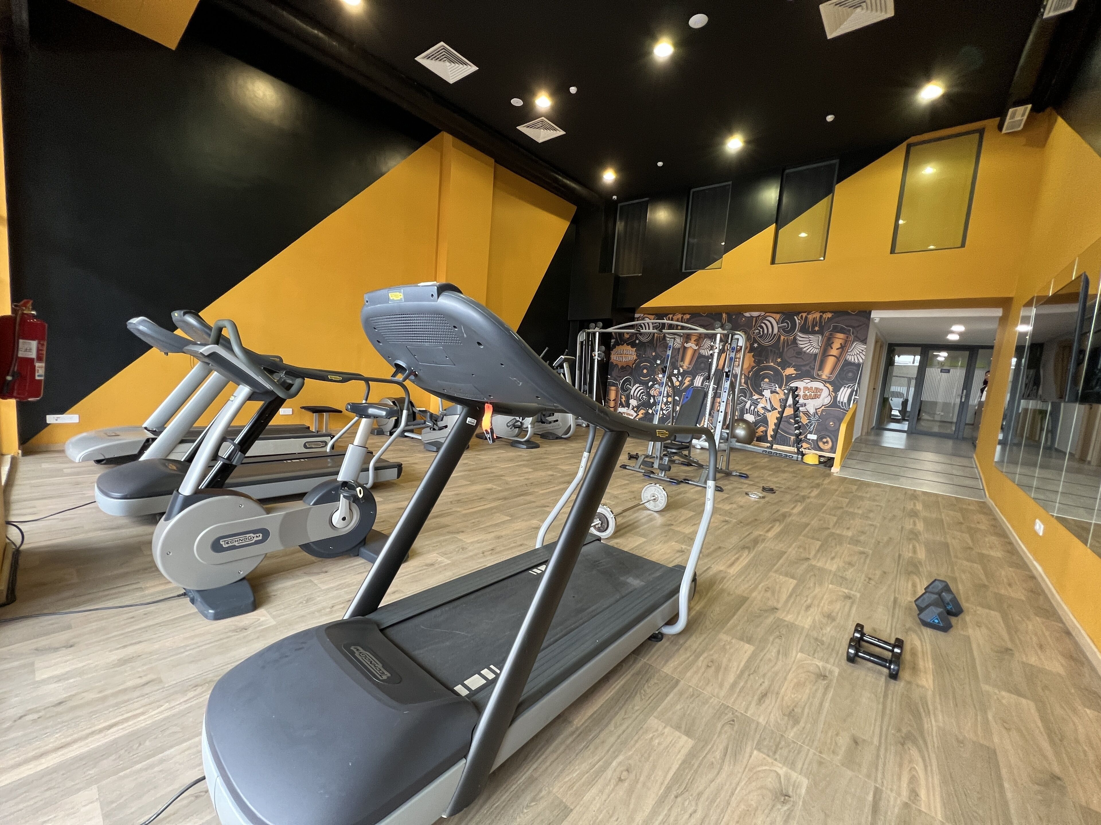 Un gimnasio con cintas de correr, máquinas de pesas y un espejo grande.