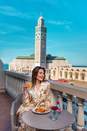A balcony with a table set for a meal, overlooking a historic building with a prominent tower. - Melliber Appart Hotel (Casablanca)