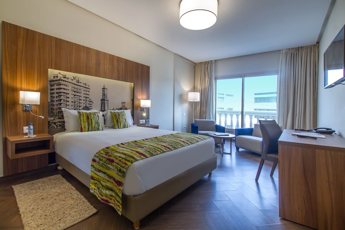 Ein Hotelzimmer mit einem großen Bett, einem Schreibtisch, einem Sessel und einem Balkon mit Blick.