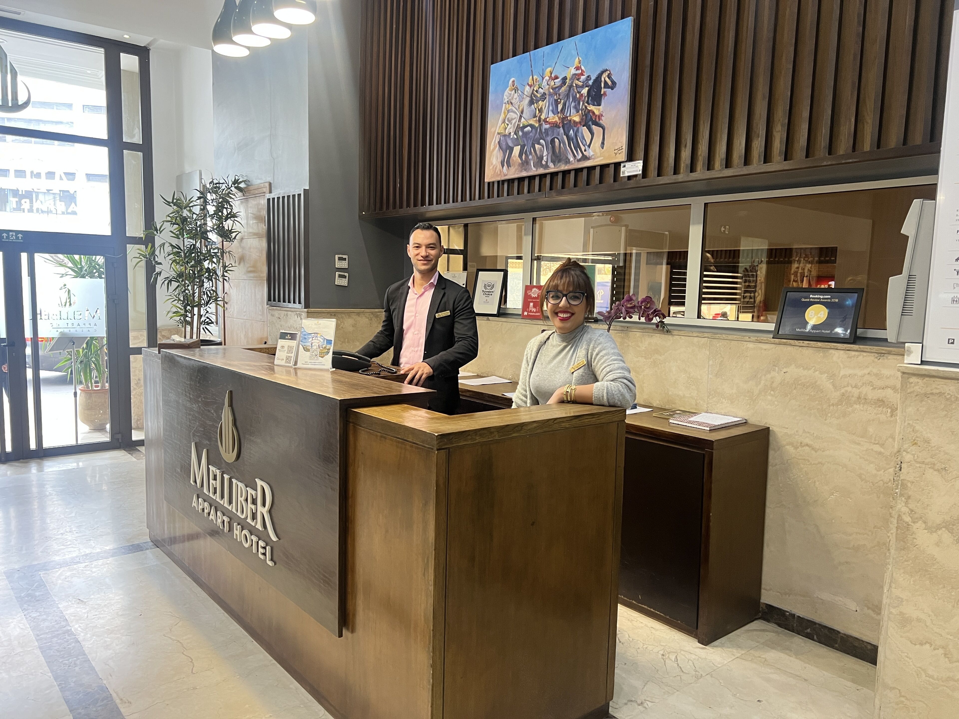 A hotel reception desk with a modern design, a large window, and a painting above the desk.