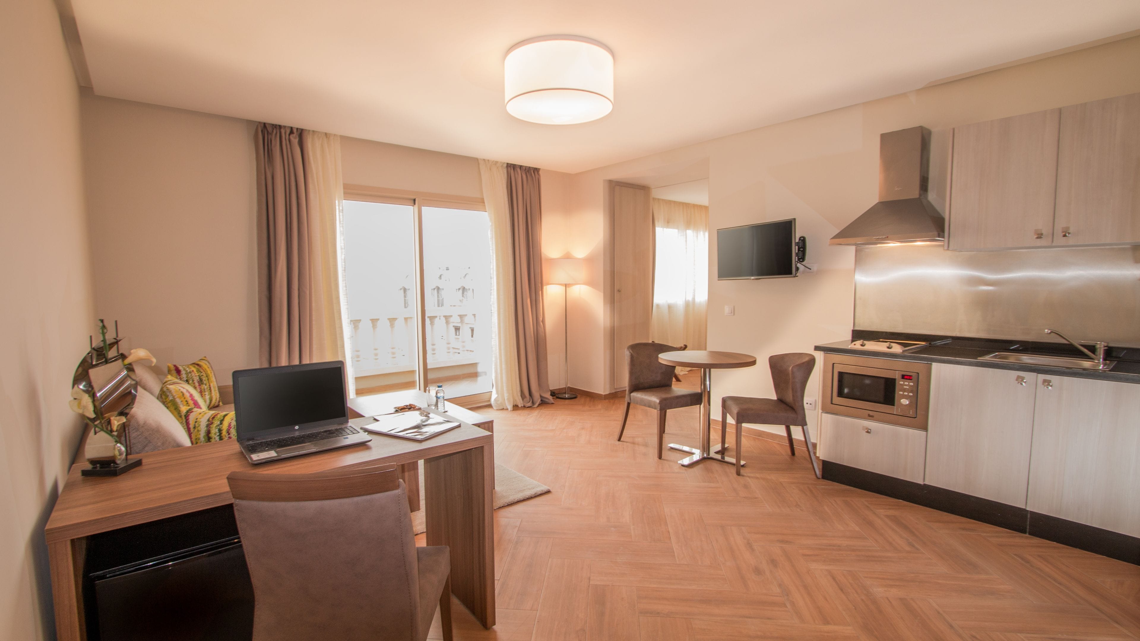 Une chambre d’hôtel moderne équipée d’une table à manger en bois, d’un ordinateur portable, d’un téléviseur à écran plat, d’un four à micro-ondes et d’une kitchenette.