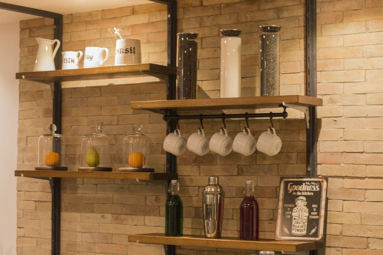 Een keuken met houten planken vol keukengerei, flessen en een bord.