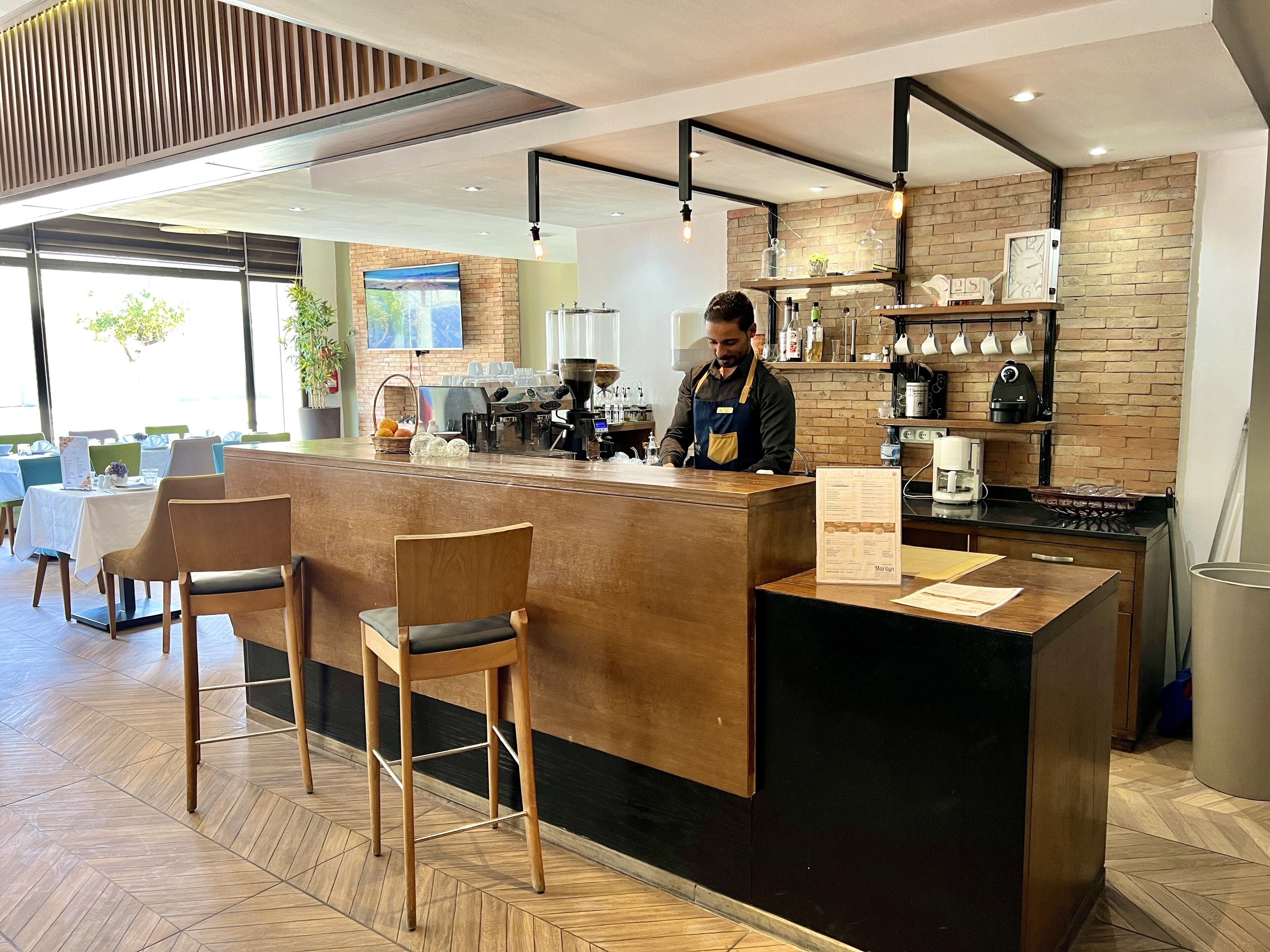 A modern coffee shop with a wooden counter, bar stools, and a brick wall.