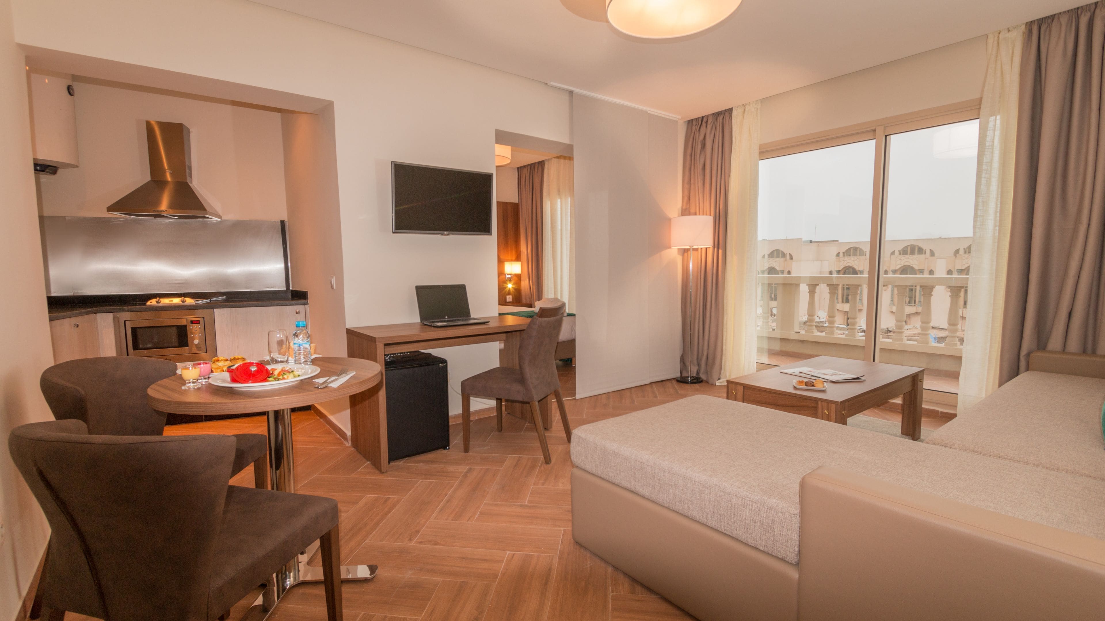 A hotel room with a bed, a desk, a chair, a sofa, a TV, and a balcony with a view.