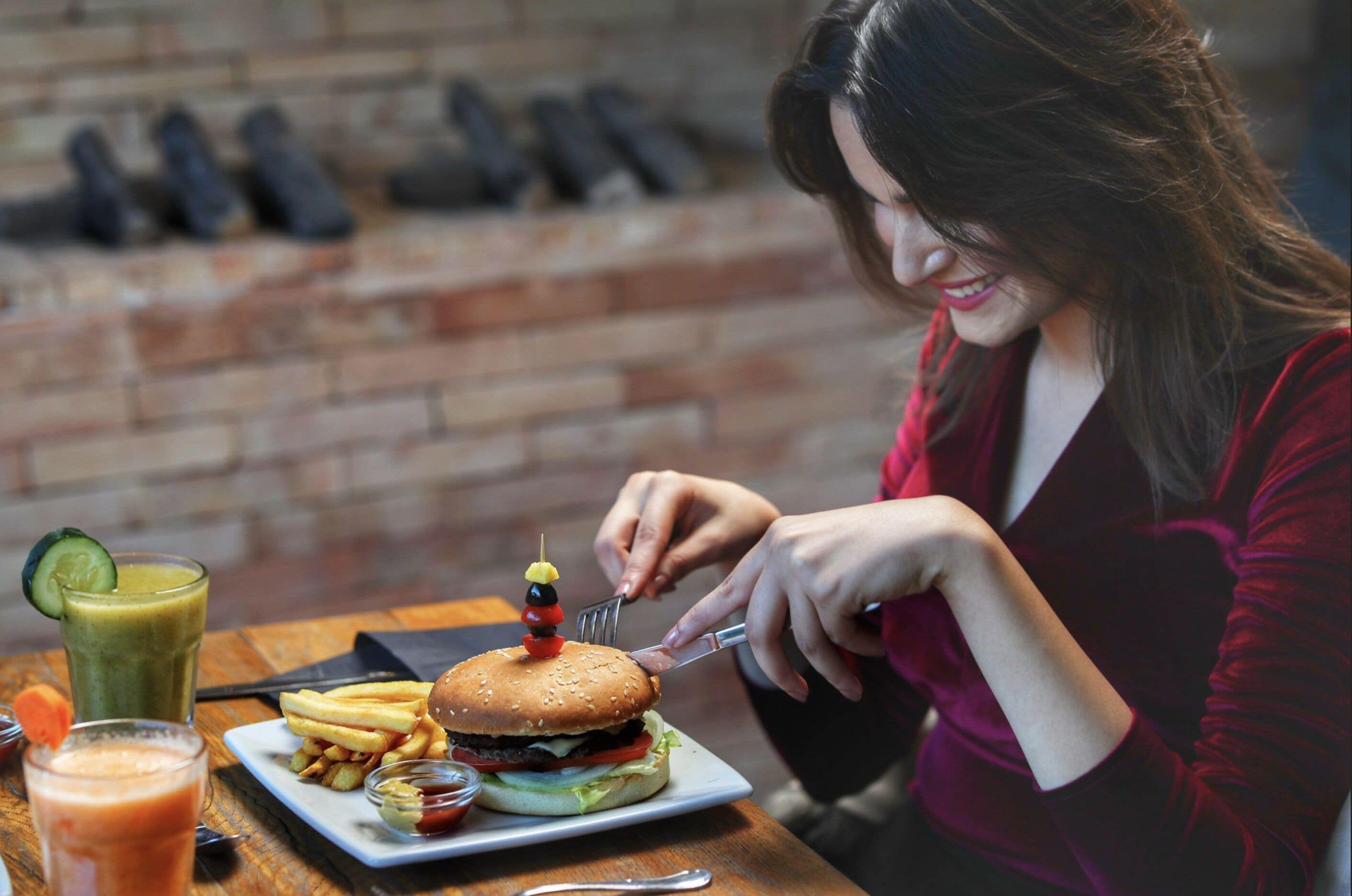A person dining at a restaurant with a burger, fries, and drinks on the table.
