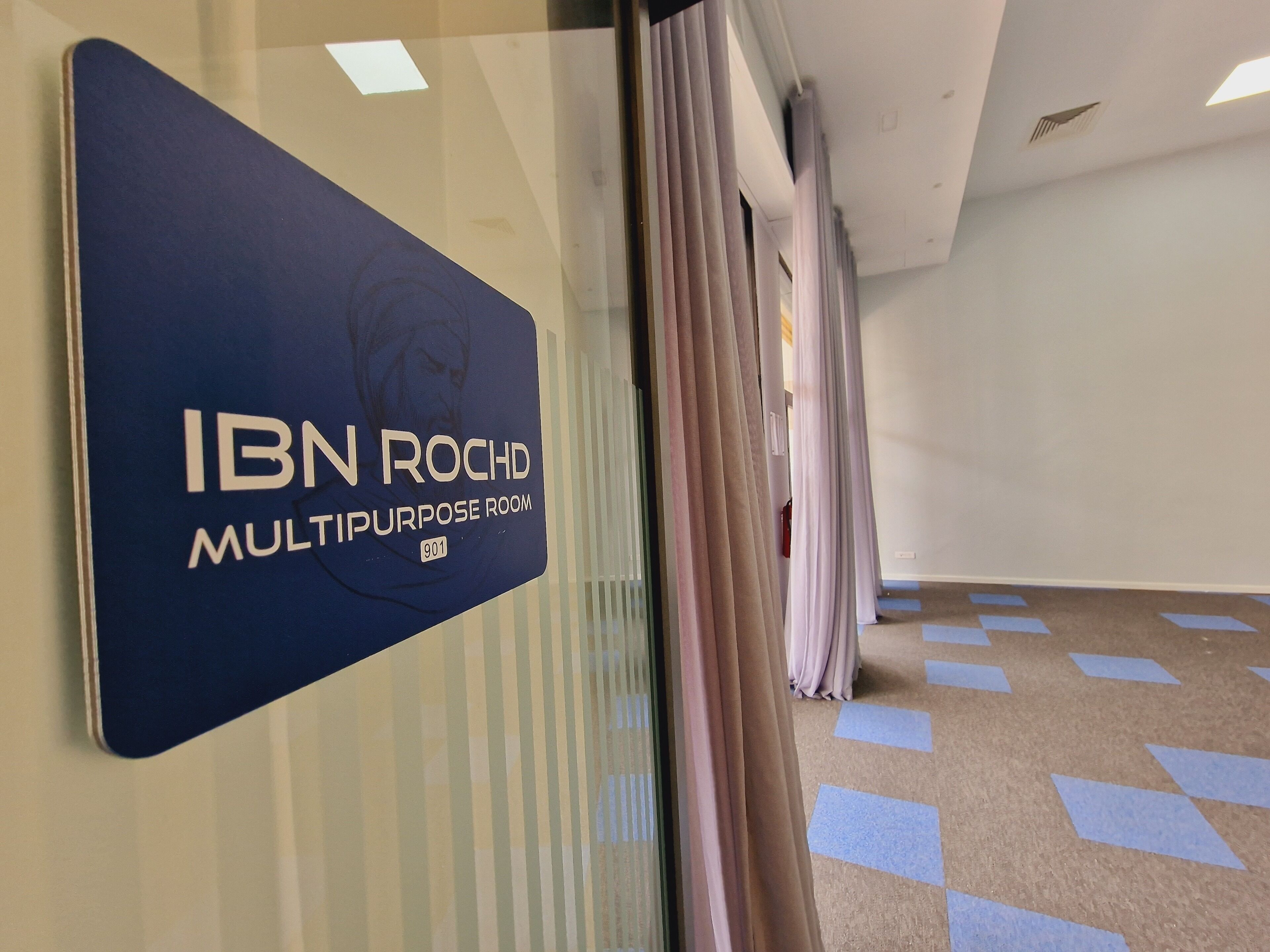 Naamplaatje voor de multifunctionele zaal IBN ROCHD, nummer 901, met een gang en een kamerbreed tapijt.