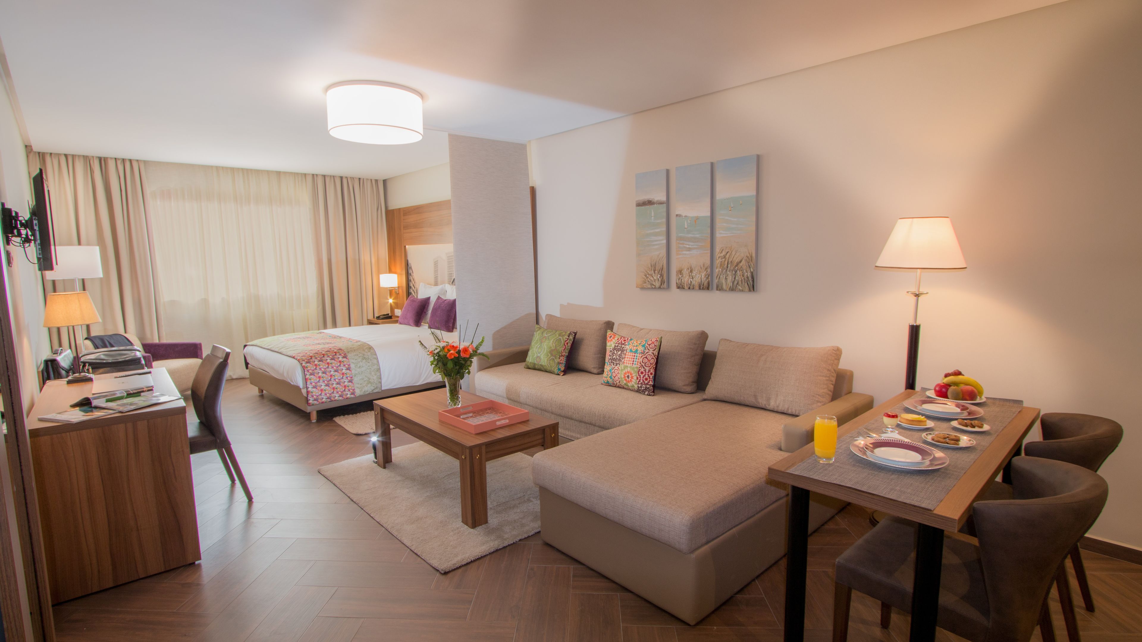 A modern hotel room with a bed, sofa, desk, and dining area.