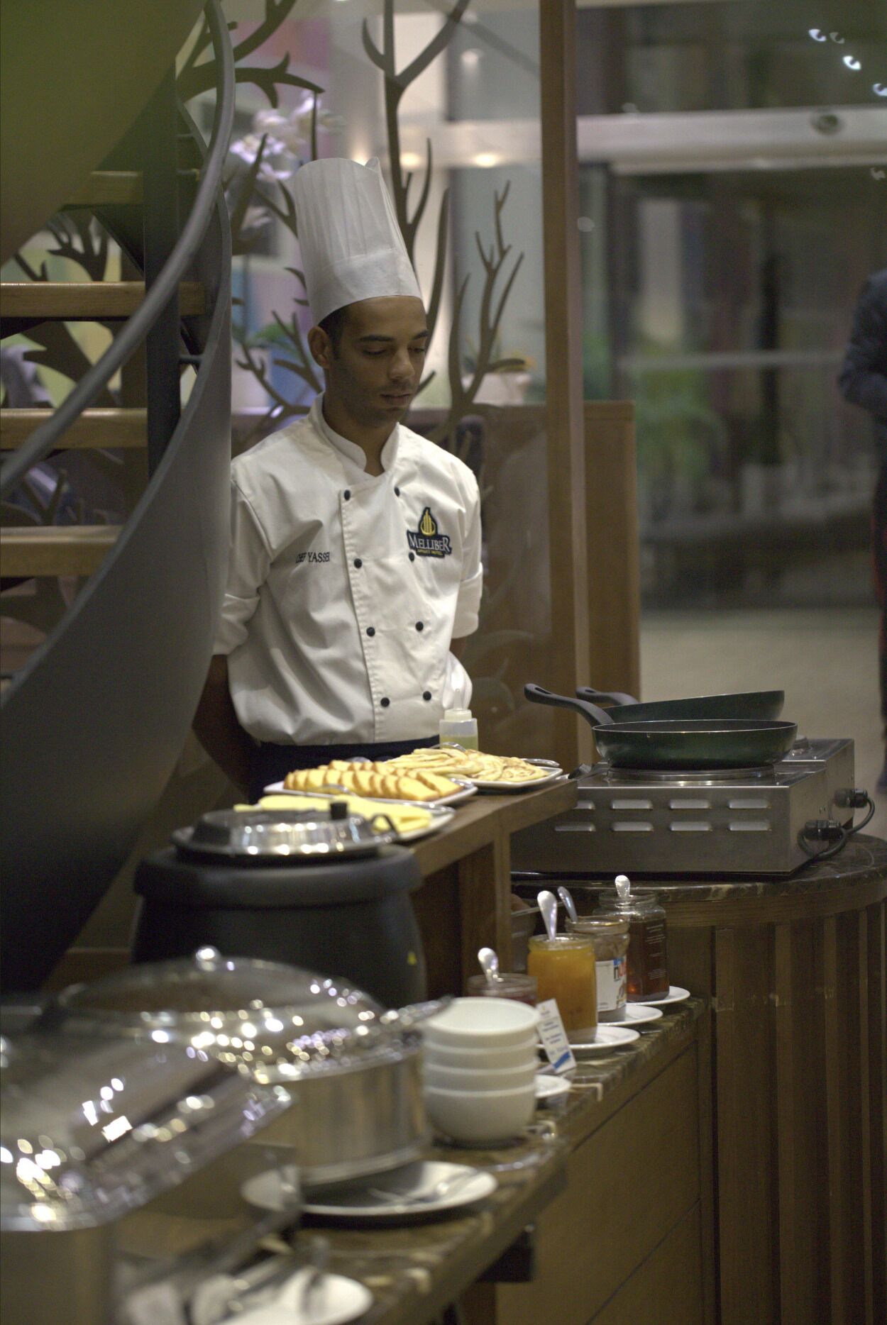 A buffet setup with a chef in uniform, a variety of dishes on trays, and condiments on the counter.