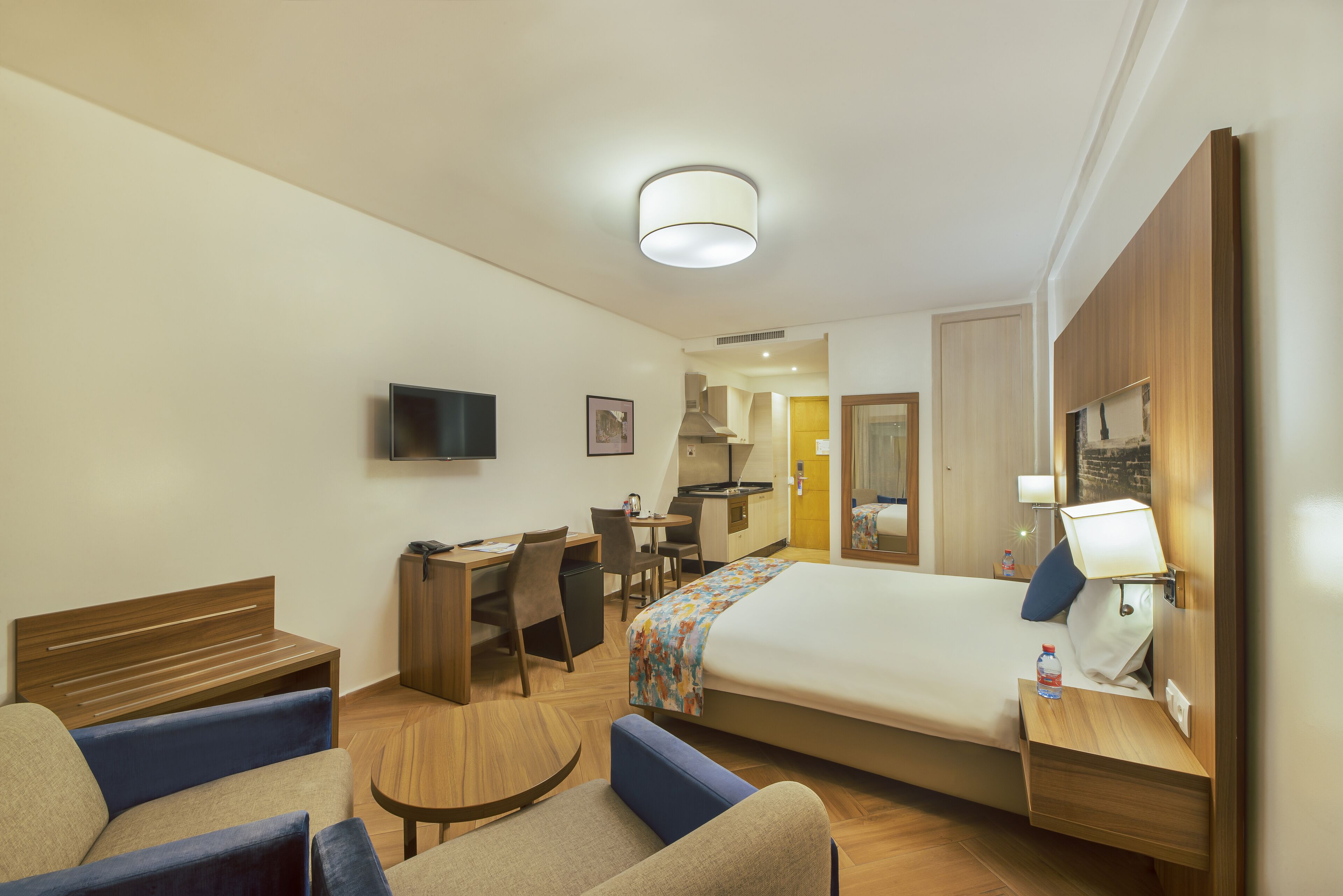 Une chambre d’hôtel équipée d’un lit, d’un bureau, d’une chaise, d’une télévision et d’une petite kitchenette.