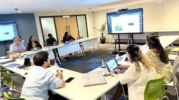 Een vergaderruimte met een lange tafel, meerdere stoelen en een groot scherm waarop een presentatie wordt getoond.