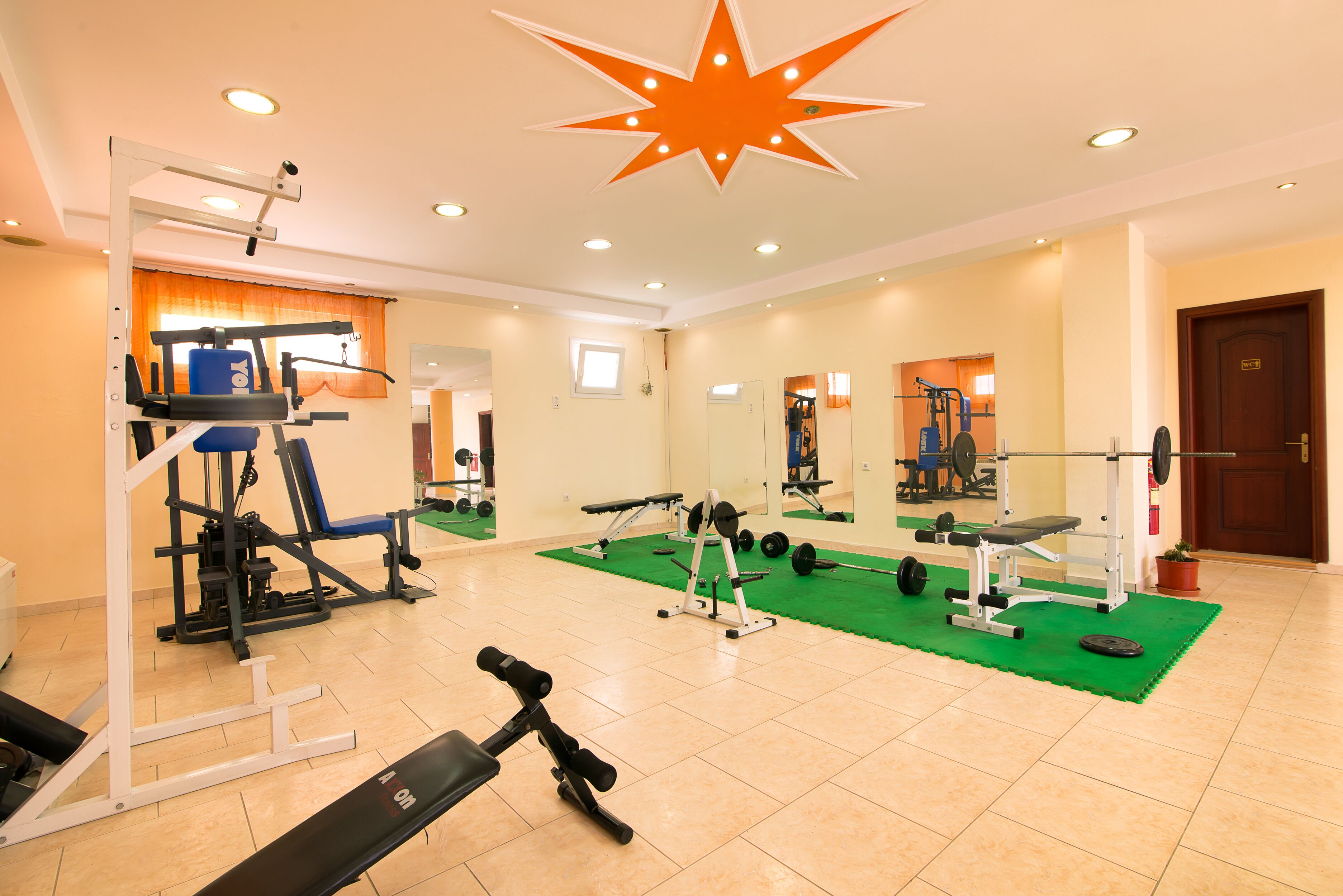 A gym with various exercise equipment, a green mat, and a large star-shaped light fixture on the ceiling.