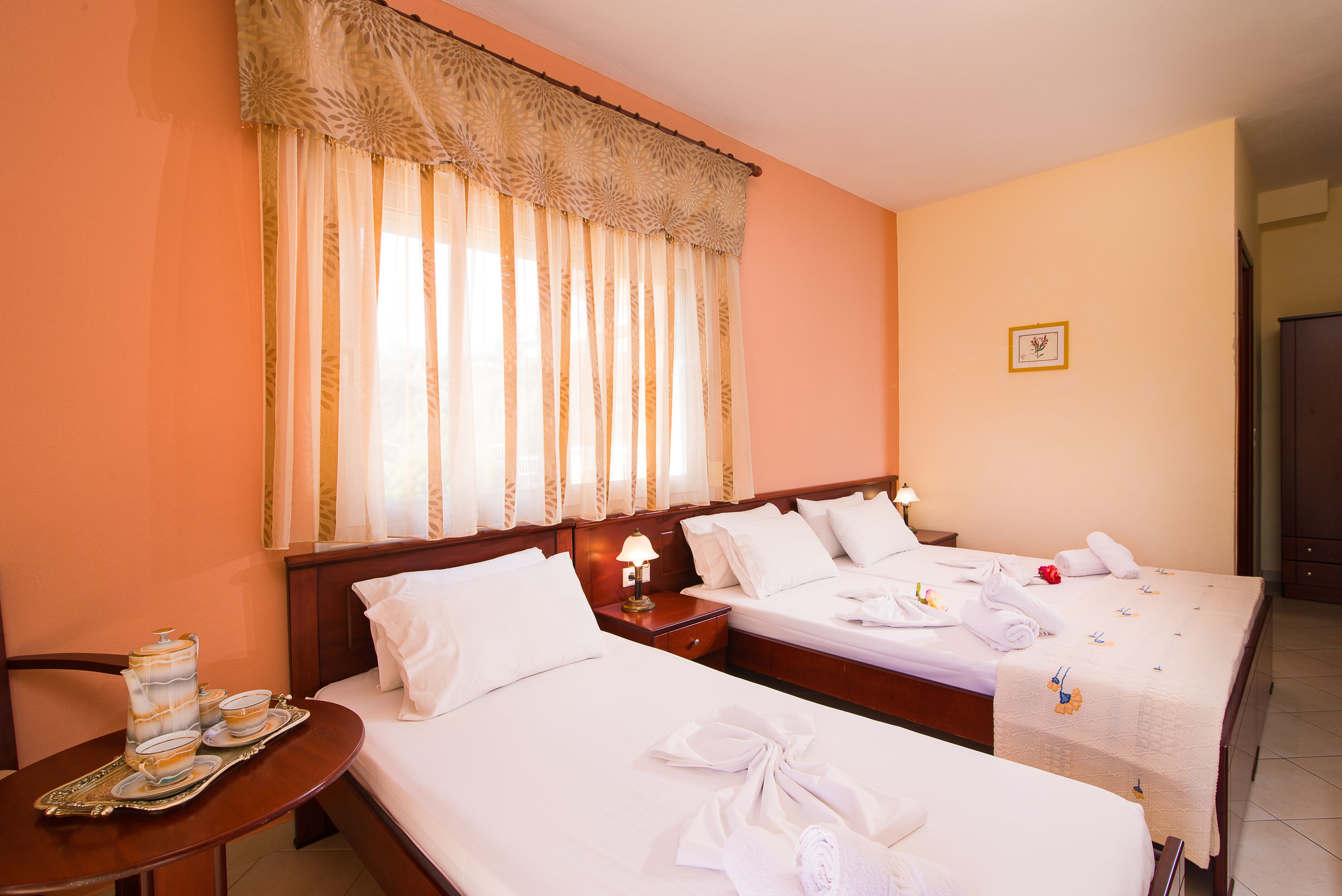 A hotel room with two beds, a nightstand with a lamp, and a tray with a teapot and cups.