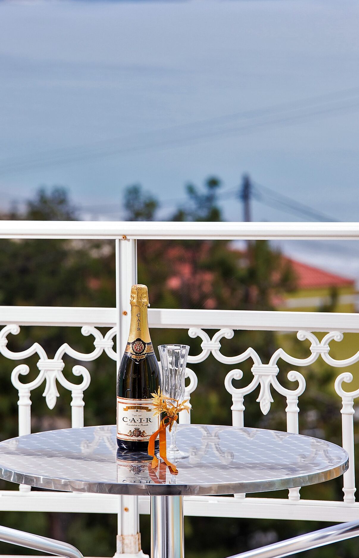 A bottle of champagne on a glass table with a white balustrade in the background.