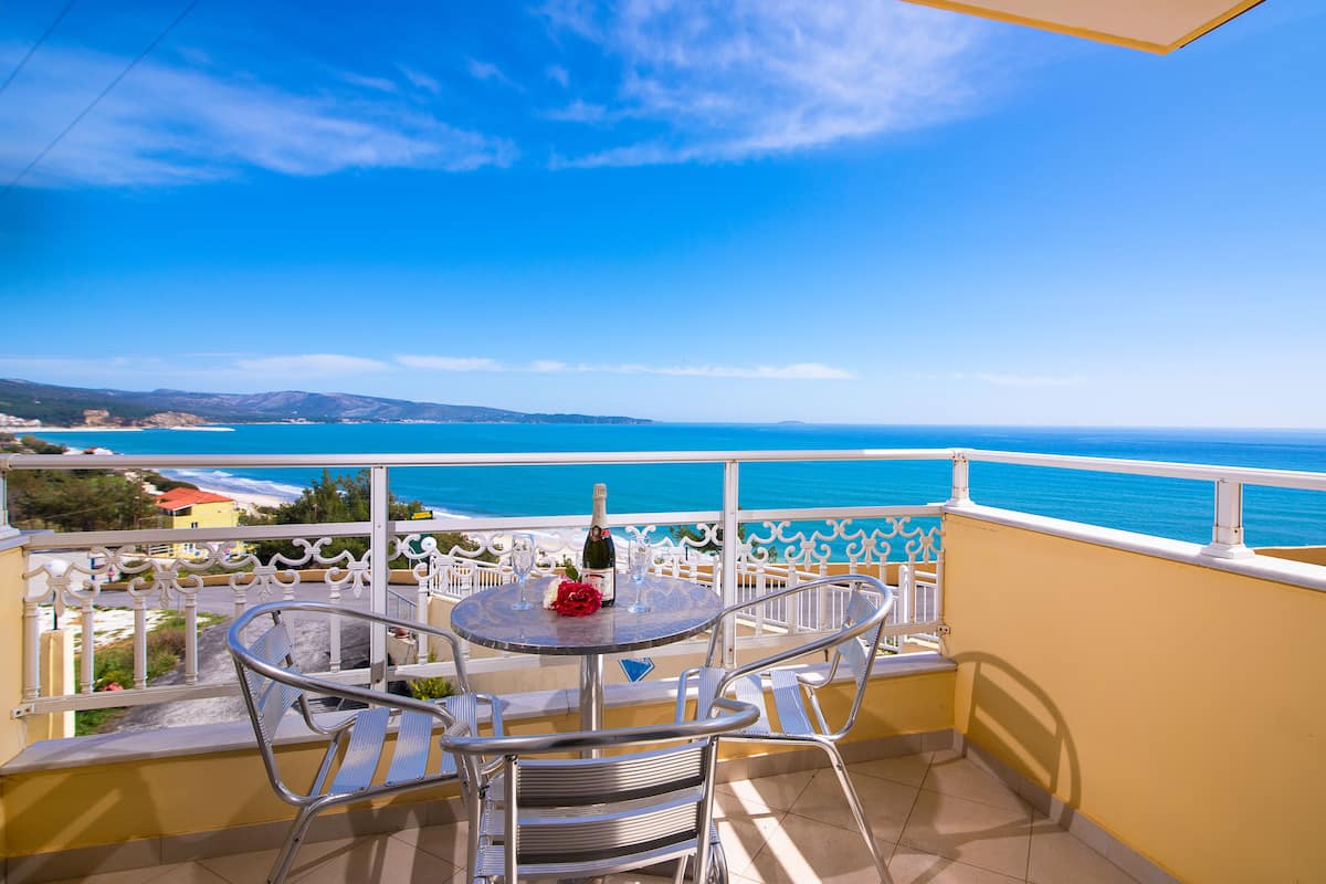 A balcony with a table and chairs, overlooking a coastal view.