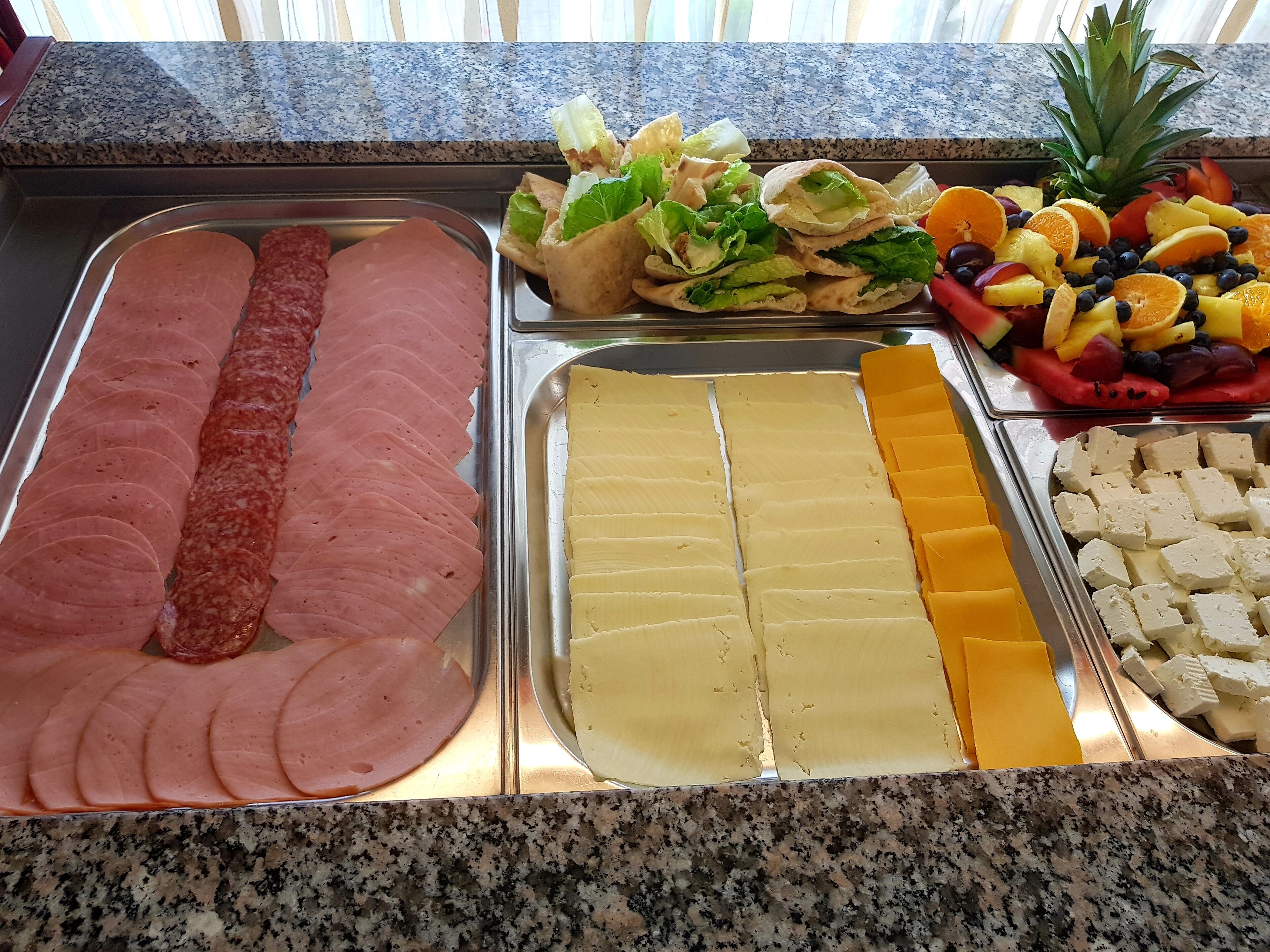 A buffet with sliced ham, cheese, and various fruits and vegetables.